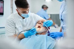 Dental hygienist cleaning a patient's teeth with instruments while the patient reclines in a dental chair.